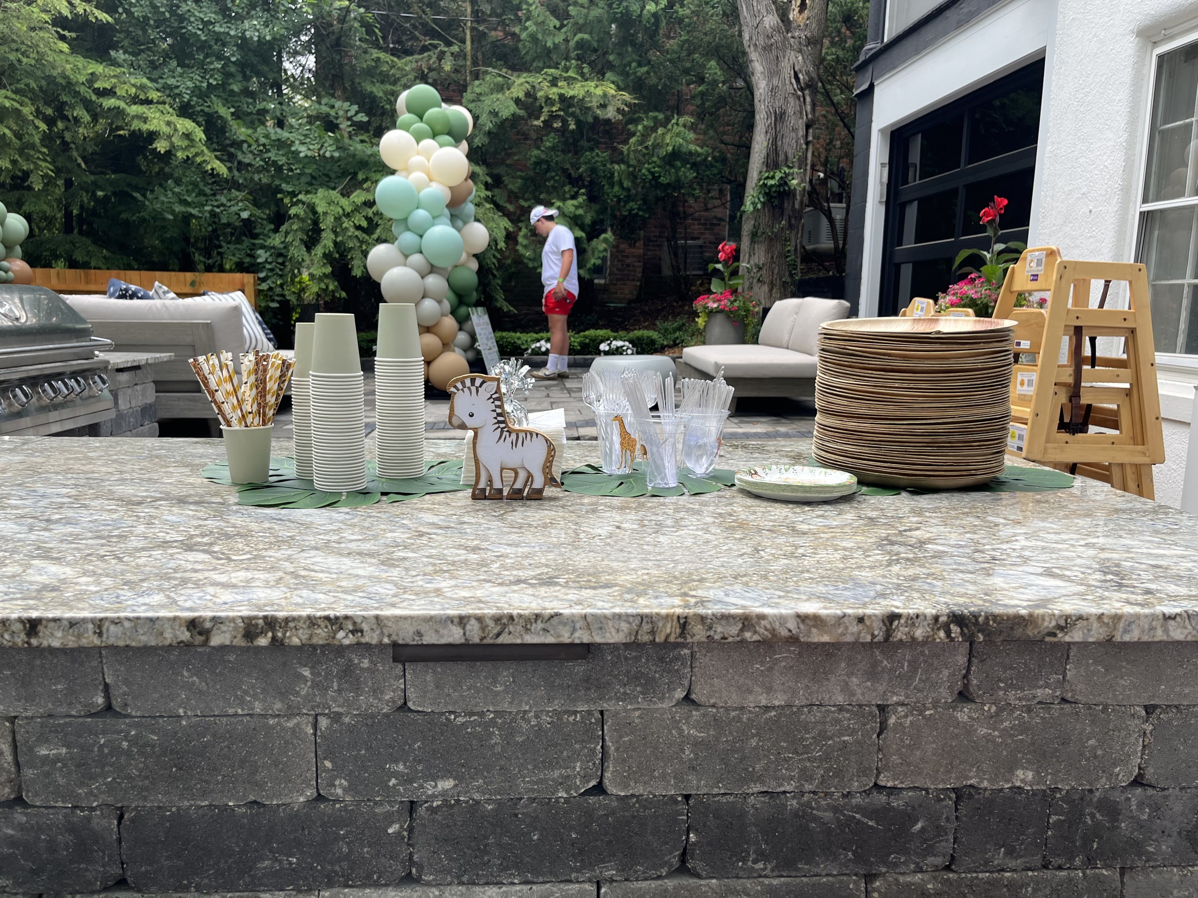 Safari birthday party outdoor drink station with sage green cups, gold paper straws, and balloon column