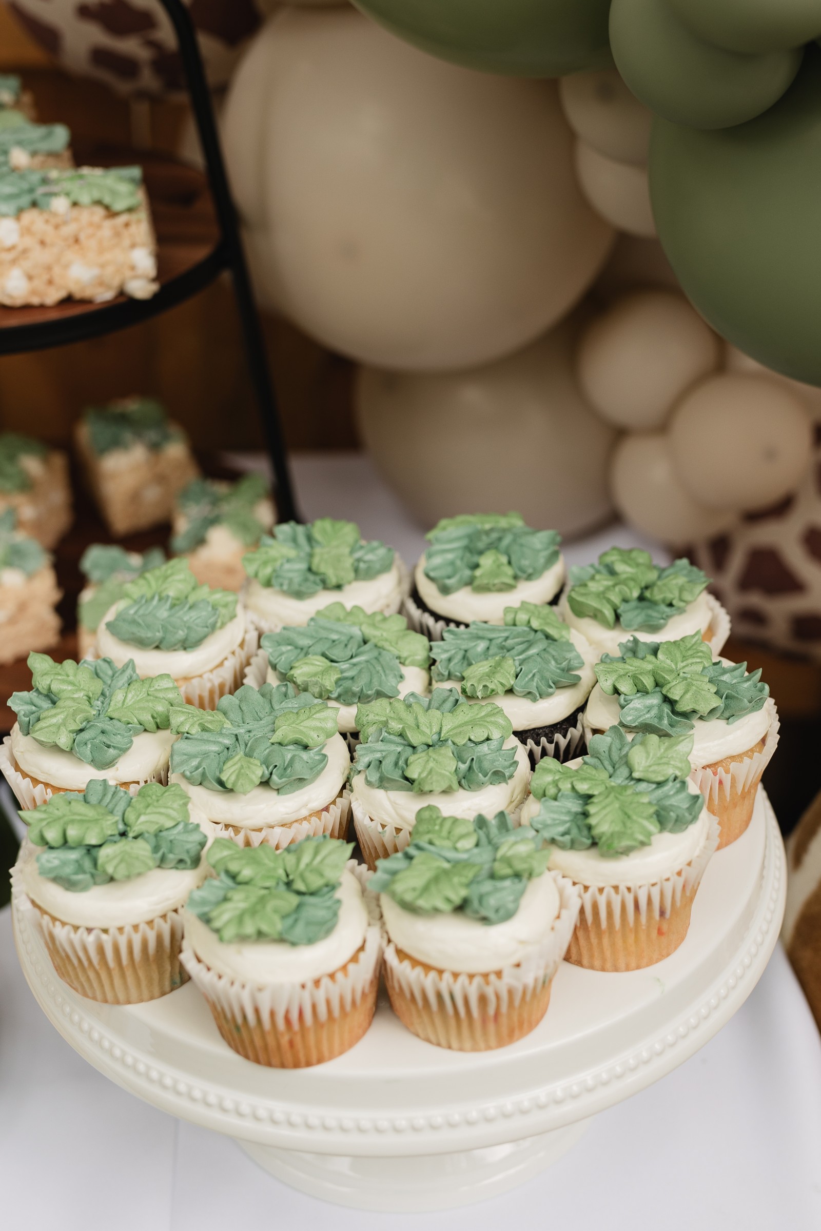 Safari birthday party cupcakes with sage green leaf frosting on a white pedestal stand